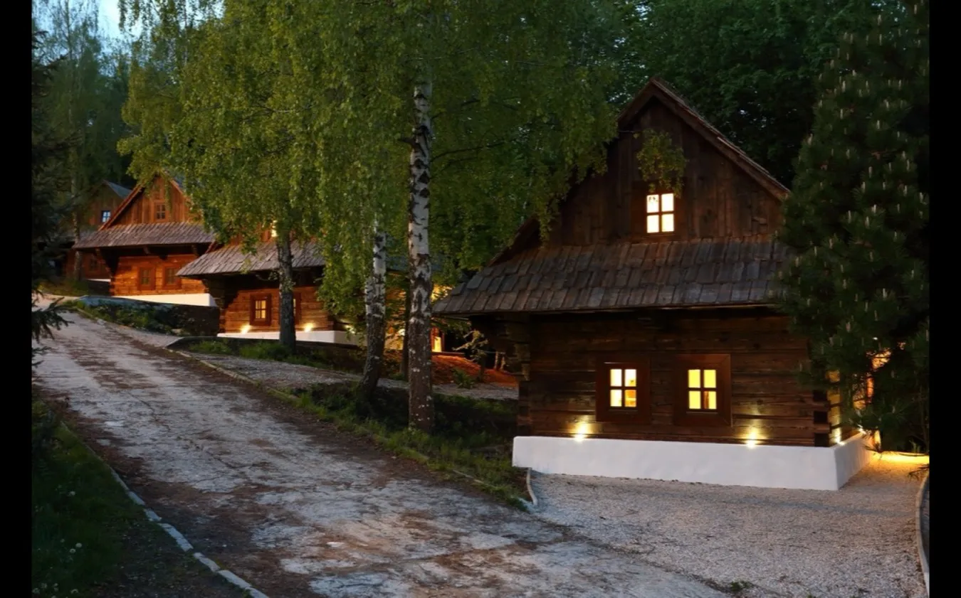 Wooden cottages lit at dusk along a path between birch trees