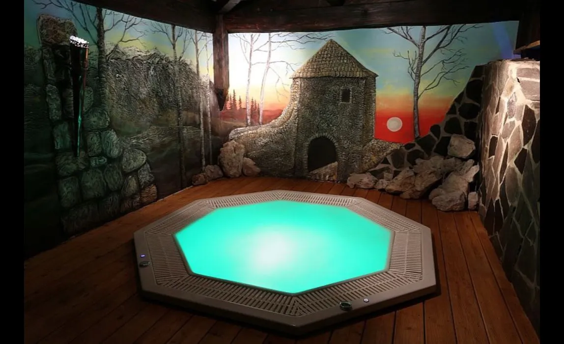 A whirlpool on a wooden terrace in front of a painted castle ruin at sunset