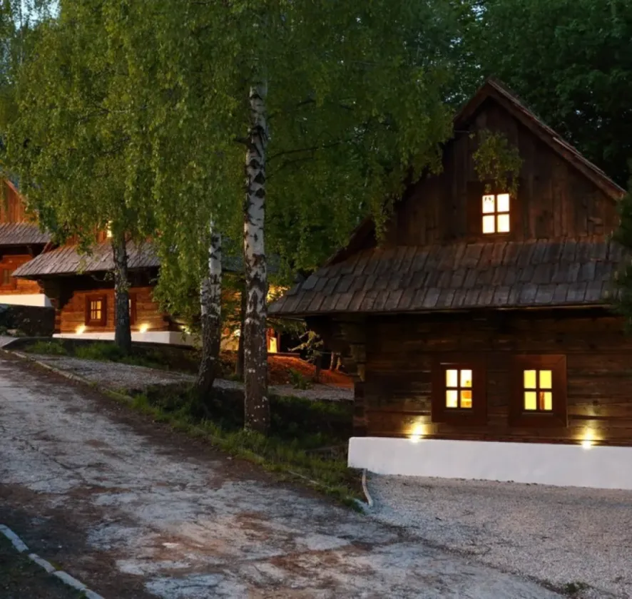 Rozsvietená drevená chalúpka medzi brezami po zotmení