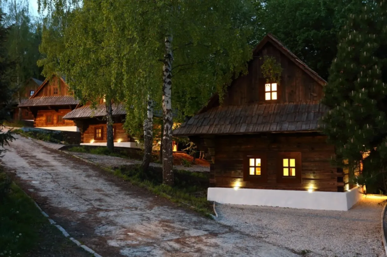 Rozsvietená drevená chalúpka medzi brezami po zotmení